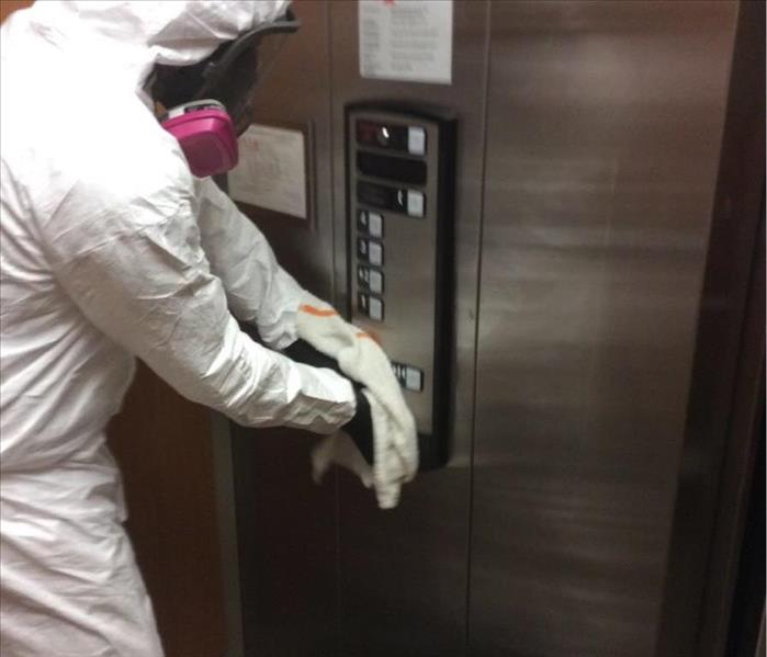 man wearing PPE wiping down elevator buttons